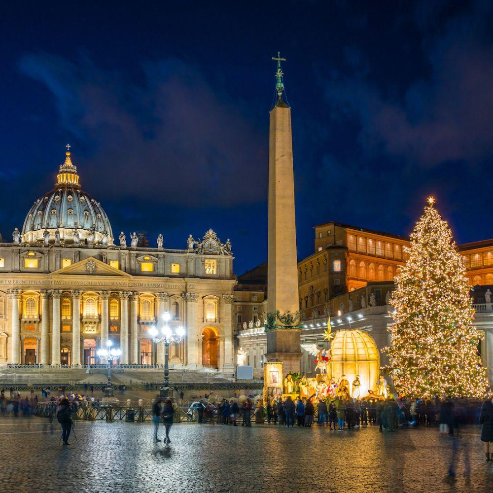 Christmas tree and Nativity scene illuminated in St. Peter’s Square at night with St. Peter’s Basilica in the background.
