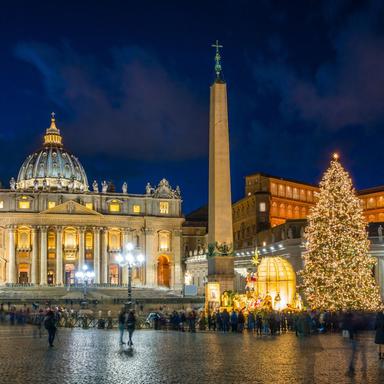 Christmas tree and Nativity scene illuminated in St. Peter’s Square at night with St. Peter’s Basilica in the background.